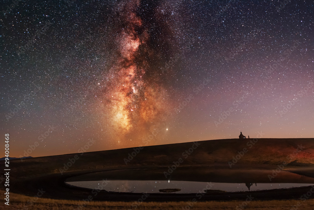 Beautiful milky way galaxy and small lake on the old volcano. On the hill small church silhouette.