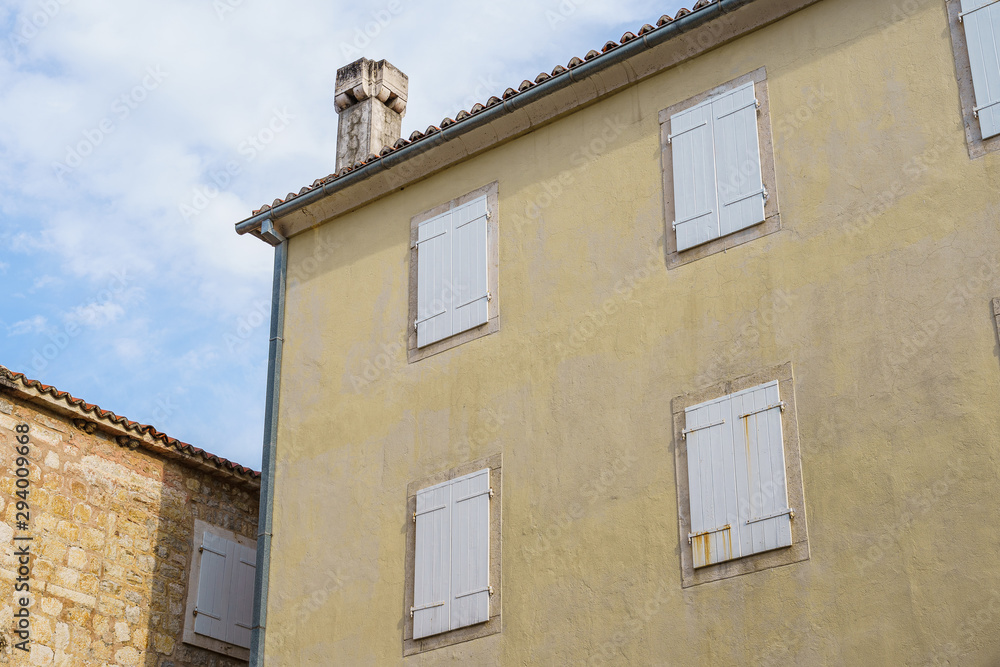 building is made of stucco stone with a tiled roof and wooden shutters on the windows