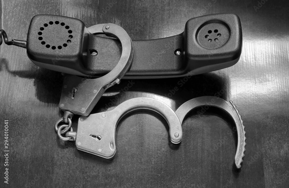 Obraz premium Phone receiver and handcuffs on wooden table