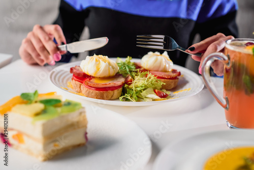 Woman eating toast with ham  tomato  poached egg and fresh salad in a restaurant. Healthy breakfast. Close-up. Space