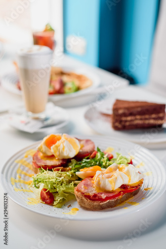 Toasts with ham, tomato and poached egg, served with fresh salad on white plate. Healthy breakfast on the table in the restaurant. Close-up. Space