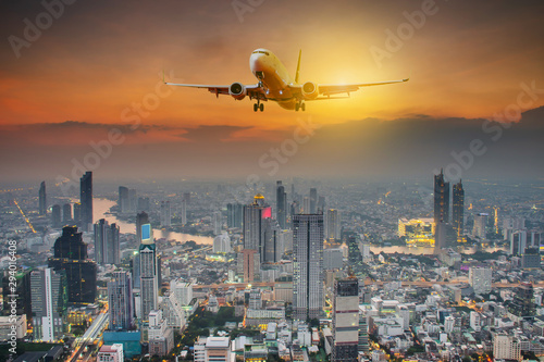 Panoramic view over the evening city during sunset, and White passenger plane flying in the sky above a city
