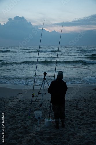 Night fishing, fisherman on the shore with sunset and sea on background, sport, competition on the Baltic Sea, vertical