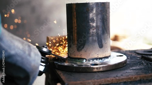 Worker with gloves working on steel pipe with angle grinder, sparkles flying around, slow motion close up photo