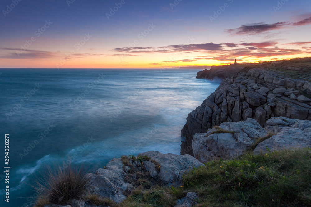 Sunrise view from a cliff in spain,near bilbao and santander, north atlantic coastline. Backlight sunlight lighting the ocean and harsh cliffs. Lighhouse in the backgrund. Very peaceful and calm mood.