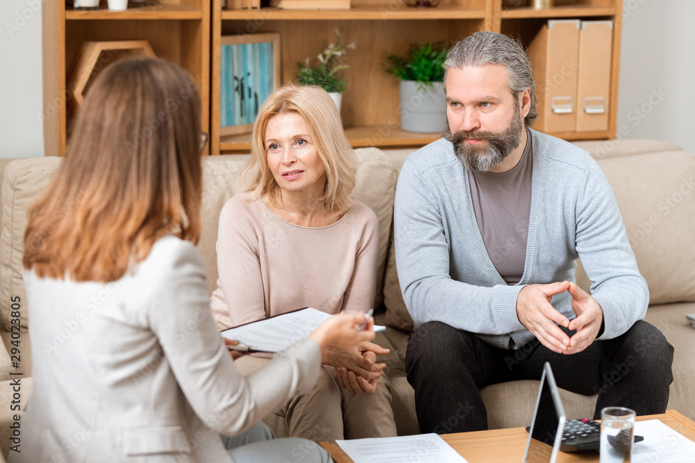 Mature man and his wife sitting on sofa and consulting with real estate agent Mature man and his wife sitting on sofa and consulting with real estate agent