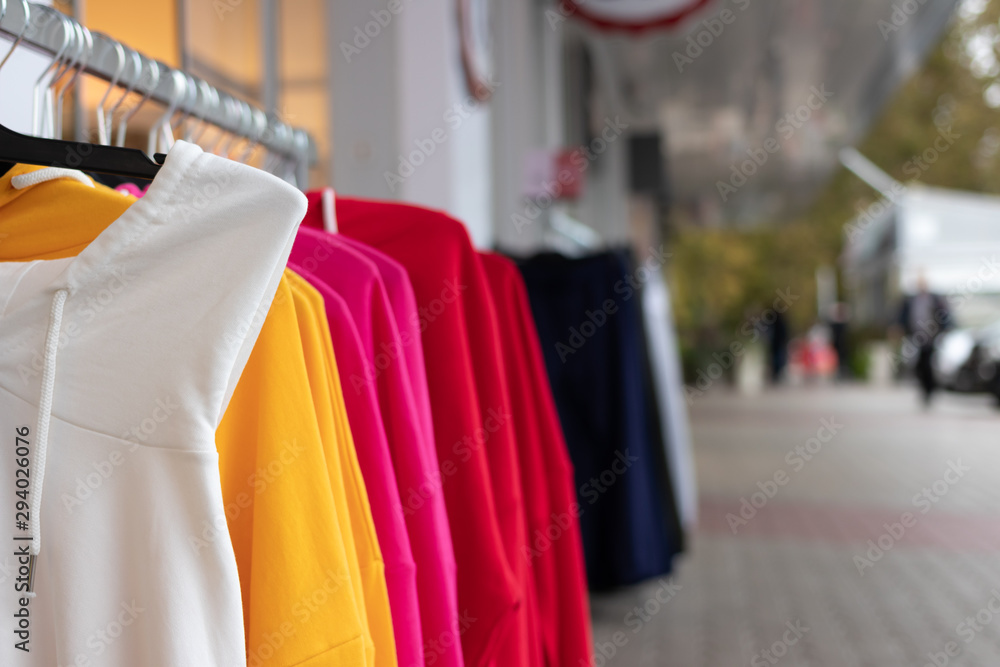 A hanger with brightly colored women's sweaters put up for sale on the street in front of the store to attract attention