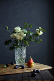 still life with white roses and fruit on a dark background.
