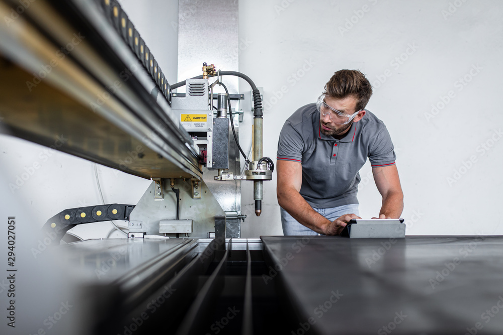 Obraz premium Young engineer setup plasma cutter for work in metalwork workshop.