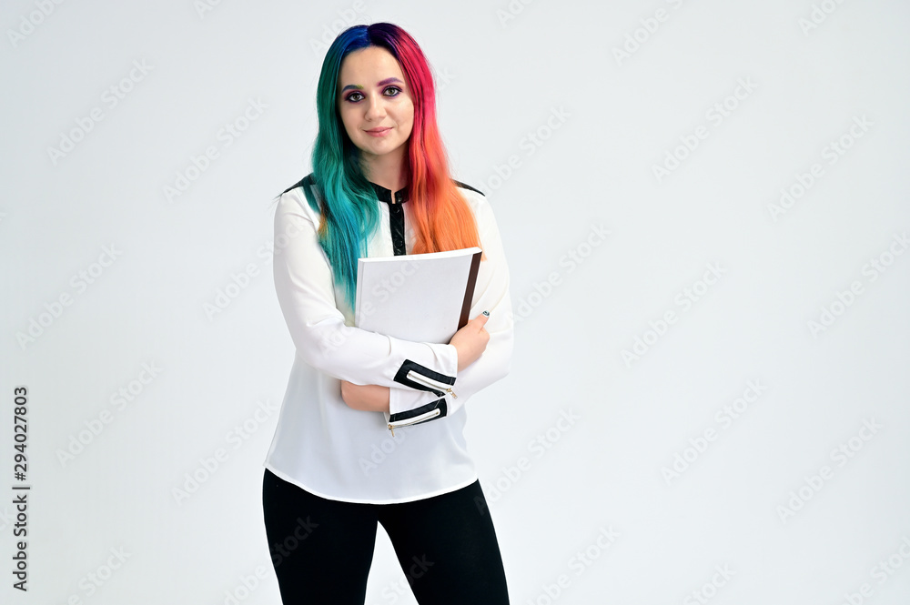 Portrait of a pretty girl in a white shirt and black jeans with multi-colored hair and makeup on a white background with a folder in her hands. Stands with a smile in various poses in the studio. Portrait of a pretty girl in a white shirt and black jeans with multi-colored hair and makeup on a white background with a folder in her hands. Stands with a smile in various poses in the studio.