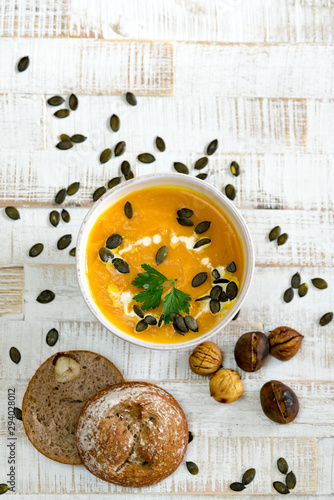 Top down view of organic pumpkin soup in a white bowl framed by chestnuts and chestnut bread and pumpkin seeds