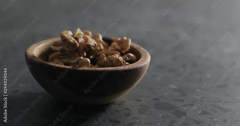 Slow motion peeled walnut kernels falling into wooden bowl on terrazzo countertop Slow motion peeled walnut kernels falling into wooden bowl on terrazzo countertop