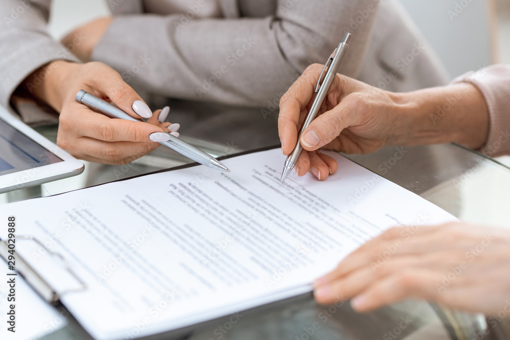 Human hands with pens over financial document in moment of putting signature Human hands with pens over financial document in moment of putting signature