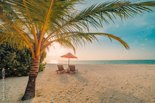 Fototapeta Naklejka Na Ścianę i Meble -  Beautiful tropical sunset scenery, two sun beds, loungers, umbrella under palm tree. White sand, sea view with horizon, colorful twilight sky, calmness and relaxation. Inspirational beach resort hotel