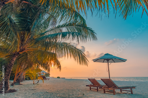 Fototapeta Naklejka Na Ścianę i Meble -  Beautiful tropical sunset scenery, two sun beds, loungers, umbrella under palm tree. White sand, sea view with horizon, colorful twilight sky, calmness and relaxation. Inspirational beach resort hotel
