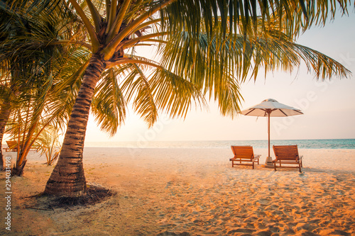 Romantic beach vacation, sunset landscape with loungers and umbrella under palm tree. Summer beach vacation concept, couple honeymoon travel destination