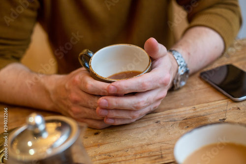 Male hands round coffee cup at wooden cafe table