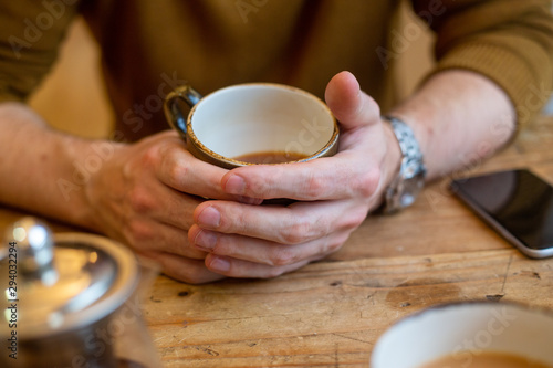 Male hands round coffee cup at wooden cafe table