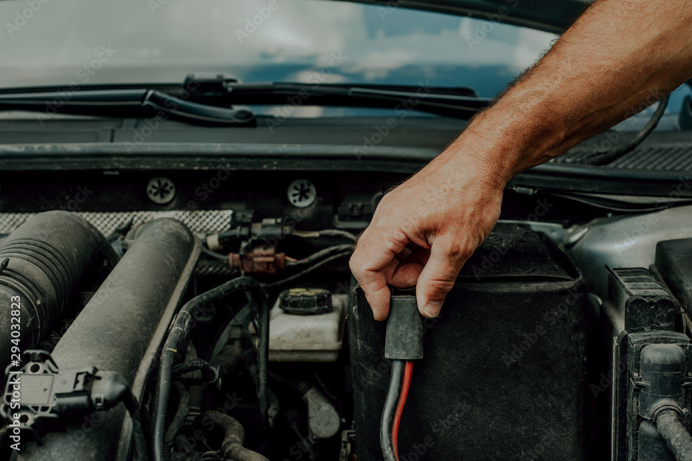Checking the battery in the car. Concept of car failure, problems with firing a car. The man checks the wires in the car's battery. Checking the battery in the car. Concept of car failure, problems with firing a car. The man checks the wires in the car's battery.