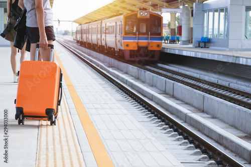 Woman tourist with orange suitcase waiting the train at train station background. travel, tourist, vacation concept.