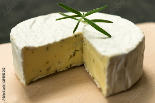  Camembert cheese with greens decorated with a sprig of rosemary on a wooden board on a black background.