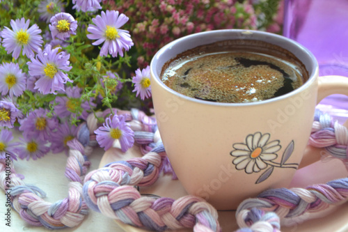 cup of coffee next to autumn purple flowers on wooden texture.