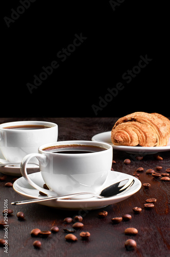 Fototapeta Naklejka Na Ścianę i Meble -  Two cups of coffee in a saucer and a croissant on a dark wooden table.