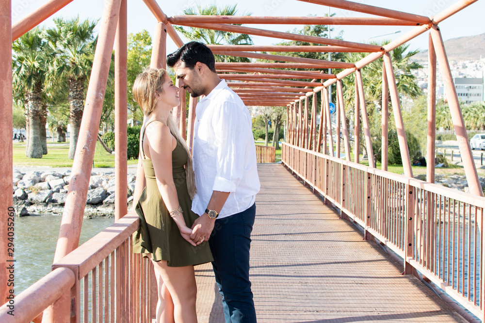 Romantic in-love and happy mixed race couple. Caucasian blonde woman and Turkish (Middle Eastern) man in love. Romantic lovers on vacation. Honeymoon in Turkey. Standing and holding hands. Eyes closed