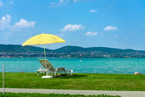 Fototapeta Stylish lounger plastic sunbed with yellow stripes sunshade beach umbrella on the green grass on beach at summer under open sky