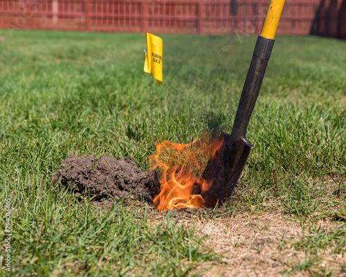 Real black smoke and flames rise from fire in hole of yard. Natural gas warning flag and shovel. Concept of notify utility locating company for underground utilities before digging and safety photo