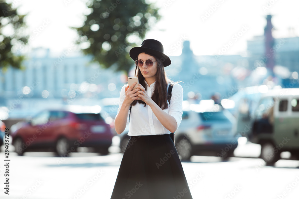 young woman in a hat and with a backpack walks in the city and uses a smartphone. young woman in a hat and with a backpack walks in the city and uses a smartphone.