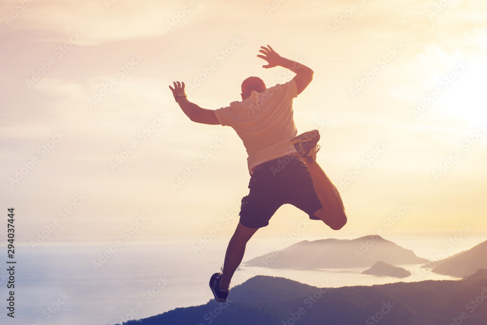 Young man hovered in a jump in the air against the seascape and mountains at sunset, rear view, toned. Concept of freedom, happiness, success. Young man hovered in a jump in the air against the seascape and mountains at sunset, rear view, toned. Concept of freedom, happiness, success.