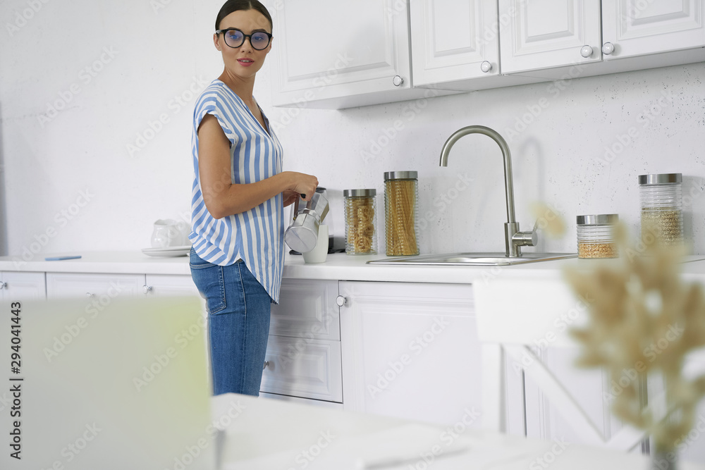 Woman with coffee pot standing in the kitchen stock photo Woman with coffee pot standing in the kitchen stock photo