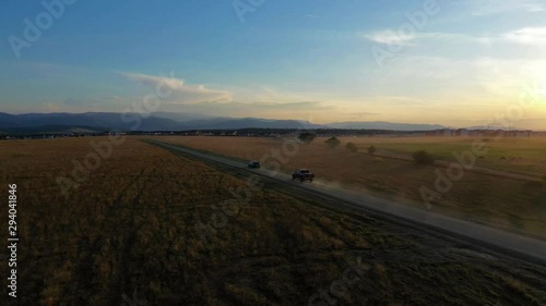 Aerial drone shot of two cars on dusty road at sunset