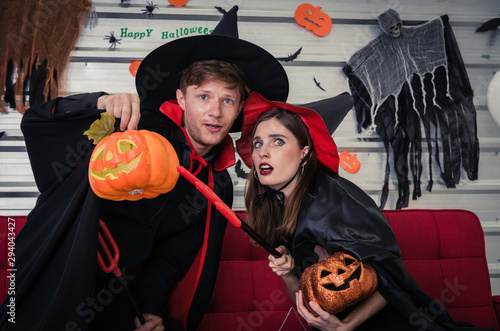 Halloween. couple young caucasian man and woman in vampires and witch clothing holding pumpkin head lantern and sitting on sofa in halloween party at home, holiday and halloween festival concept