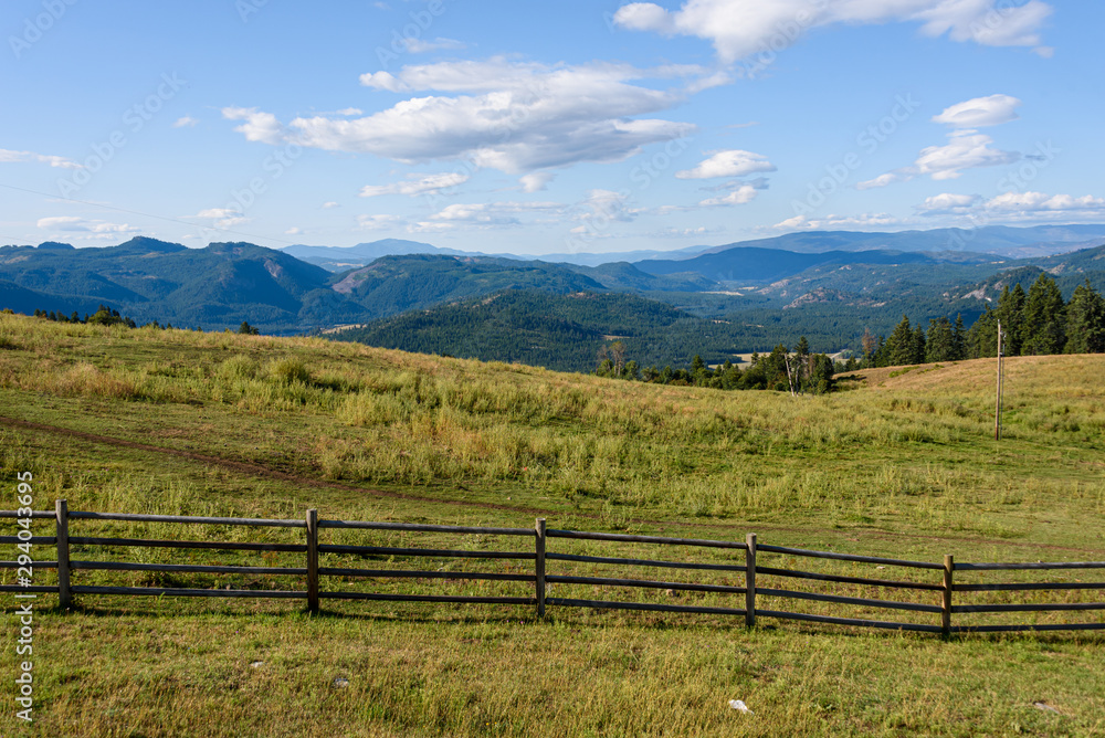 Tranquil scene in early morning light of hilltop pasture with wood fence line and sky and mountains in background
