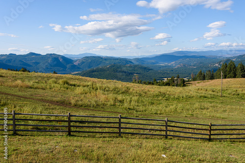 Tranquil scene in early morning light of hilltop pasture with wood fence line and sky and mountains in background