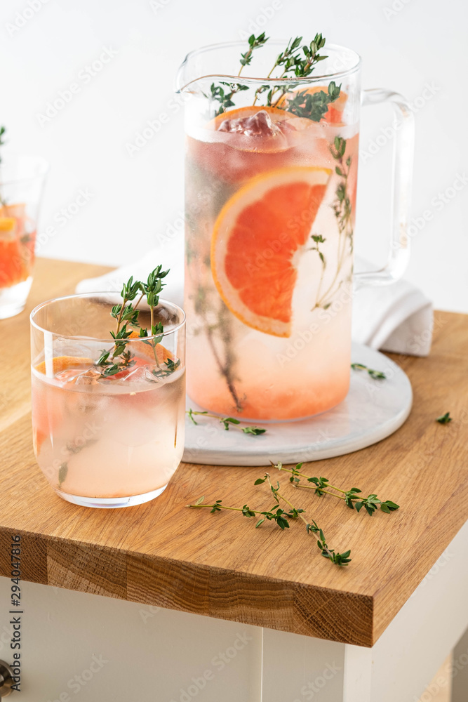 Lemonade with grapefruit and thyme in a glass jug on light background. Lemonade with grapefruit and thyme in a glass jug on light background.