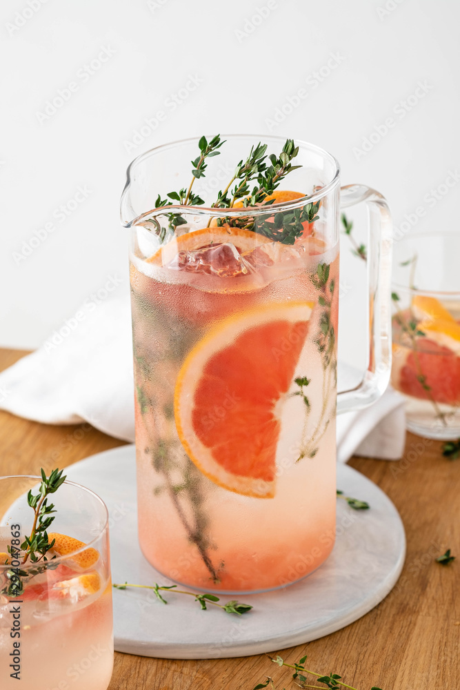 Lemonade with grapefruit and thyme in a glass jug on light background. Lemonade with grapefruit and thyme in a glass jug on light background.