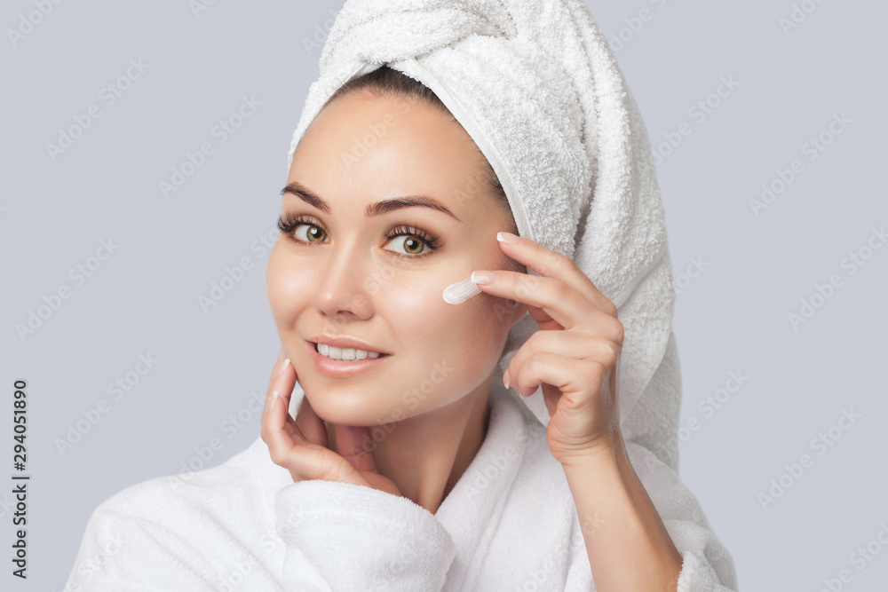 Portrait of a beautiful young woman, she applies cream to her face after a shower. Facial and body care. Portrait of a beautiful young woman, she applies cream to her face after a shower. Facial and body care.