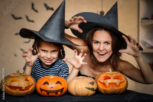 Happy family: mom and daughter celebrate Halloween. Merry people in carnival costumes in the room. Cheerful kids and parents play with pumpkins and black witch hats