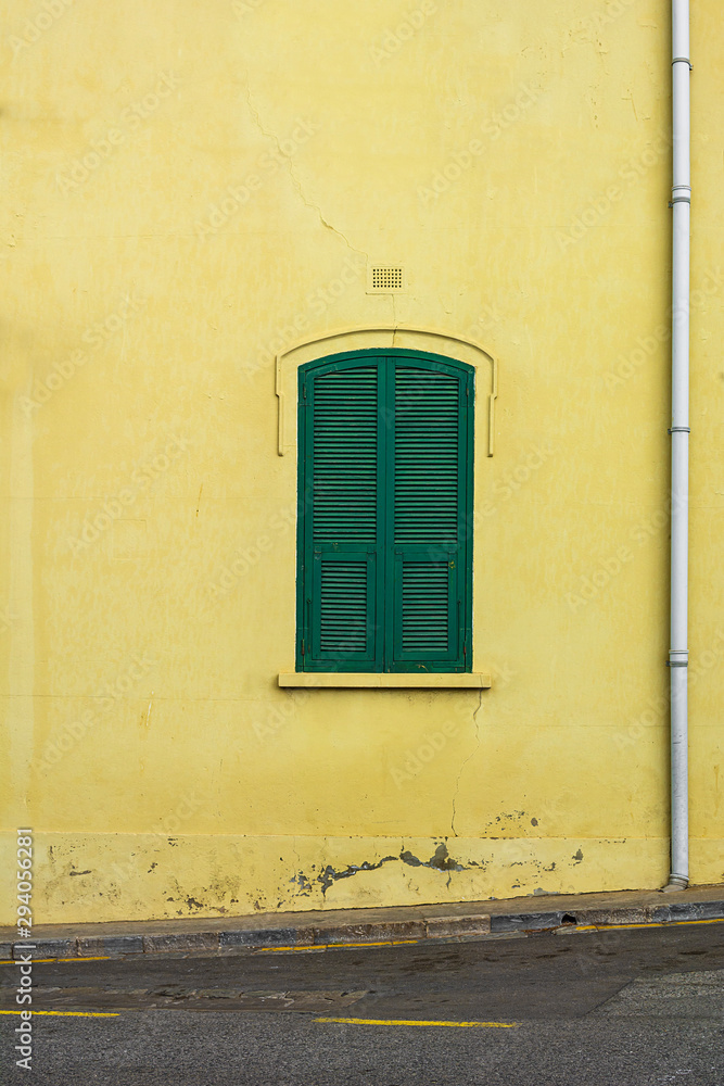 Little green window shutters on a pastel yellow wall shot straight on.