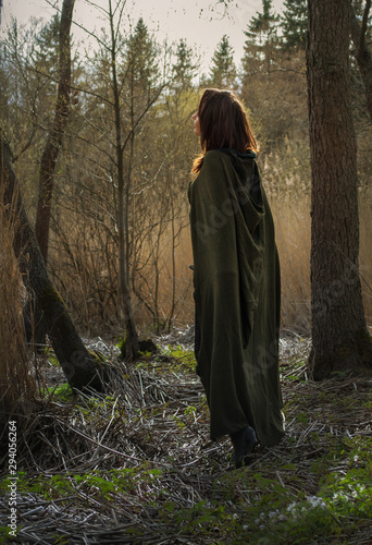 Young witch with green gloak stay in forest