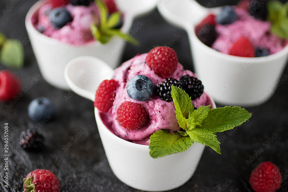 Homemade berry sorbet in white cups and fresh berries on a black background. - obrazy, fototapety, plakaty 