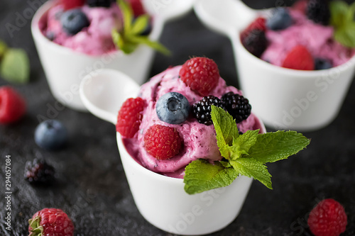 Homemade berry sorbet in white cups and fresh berries on a black background.