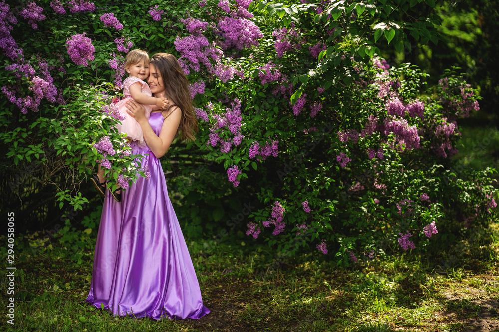 Authentic mother is holding on hands her little daughter. They standing among flowering trees. Copy space Authentic mother is holding on hands her little daughter. They standing among flowering trees. Copy space