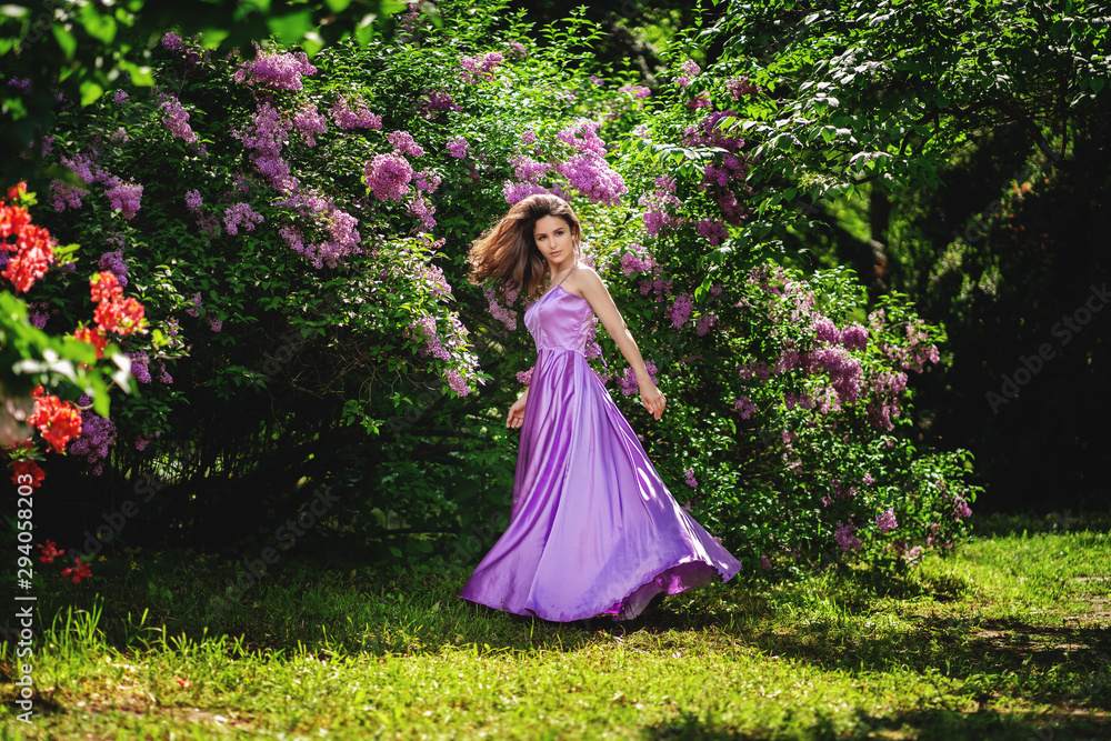 girl with in a long dress spinning in a blooming orchard, young woman smiling