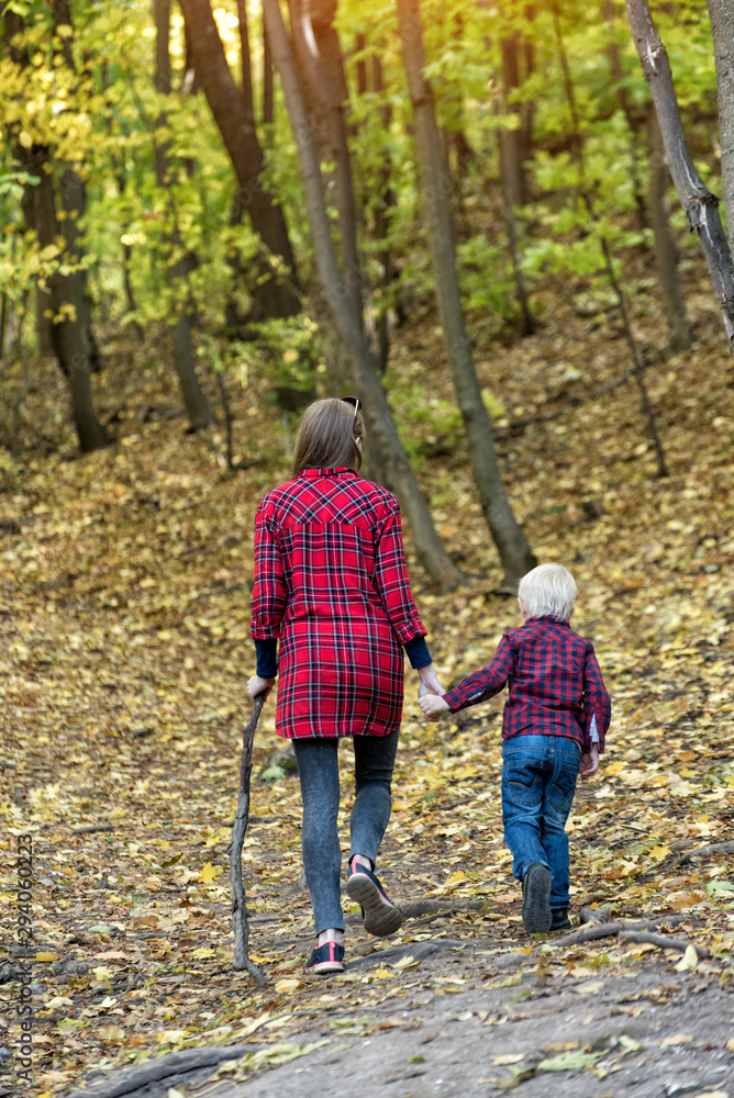 Mom and little son walk in the autumn forest. Back view Mom and little son walk in the autumn forest. Back view