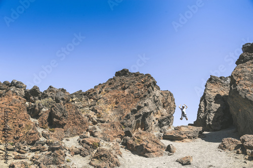 Teen jumping with raised arms in the middle of big volcanic rocks. Natural panorama with a little boy leaps happy. Teenager playing alone outdoor. Youth freedom carefree happiness and outdoors concept