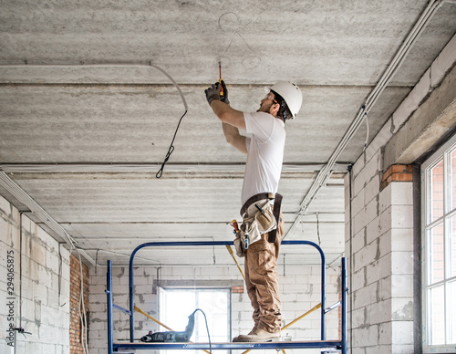 Electrician installer with a tool in his hands, working with cable on the construction site.